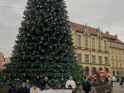 Uczestnicy i kadra obozu z bannerem FAR na rynku w Wrocławiu. W tle ogromna, udekorowana świątecznie choinka. Obóz Aktywnej Rehabilitacji we Wrocław 20-31.01.2025 r.