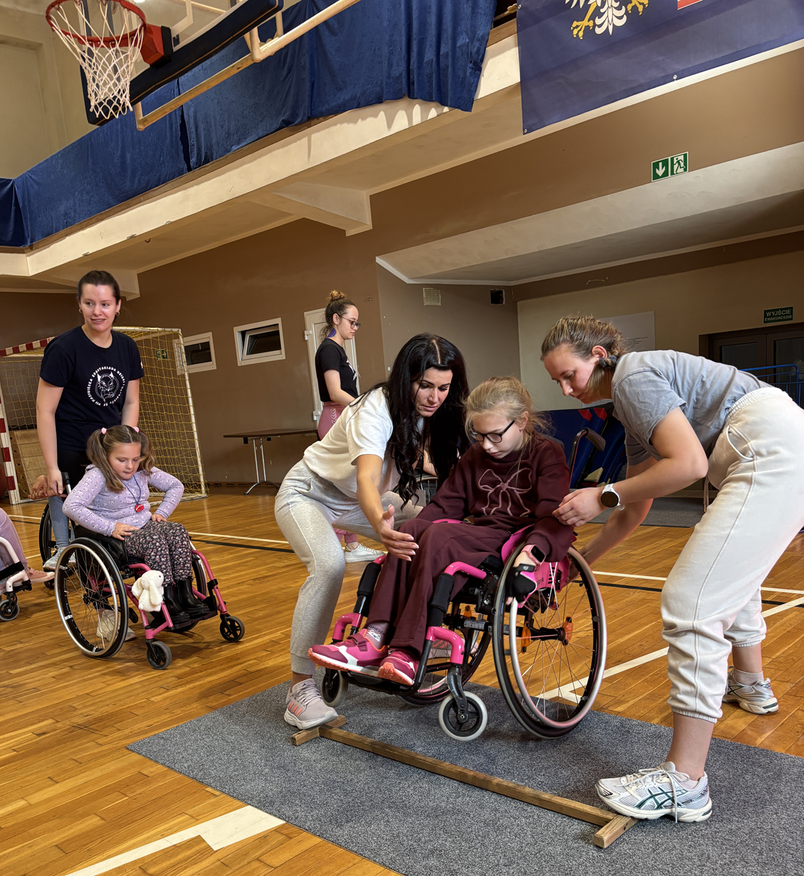 Zajęcia na sali z techniki jazdy na wózku - nauka pokonywania progu. Obóz Aktywnej Rehabilitacji dla dzieci w Cetniewie 21-30.09.2025 r.